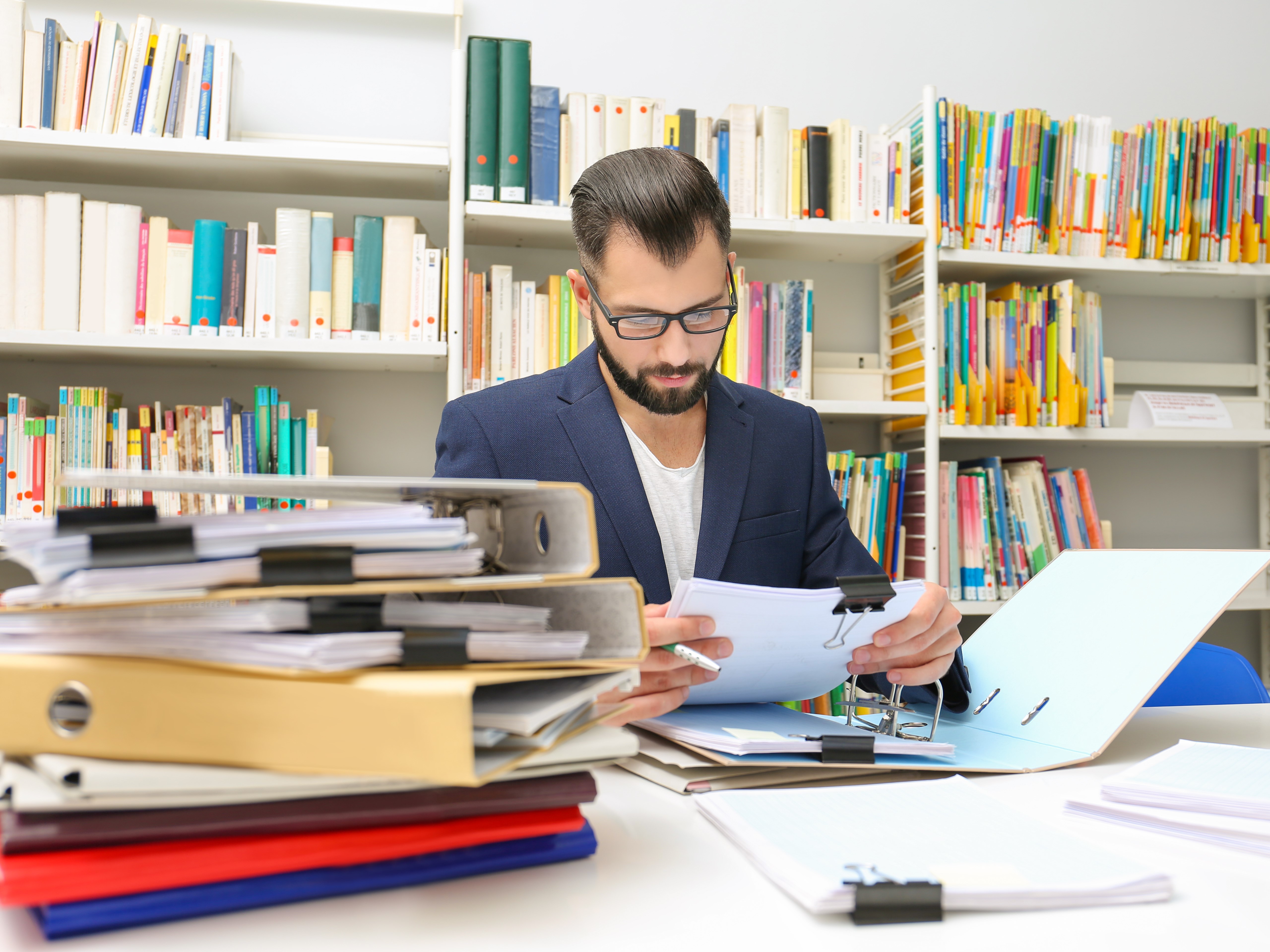 Homme avec des lunettes lisant des livres dans une bibliothèque.